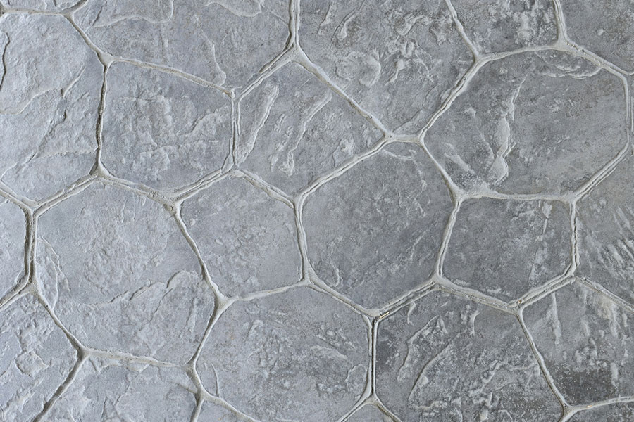 Gray stone tiles arranged in an irregular hexagonal pattern, with visible grout lines and textured surfaces that closely resemble natural stone, creating the sophisticated look of stamped concrete while maintaining authentic character.